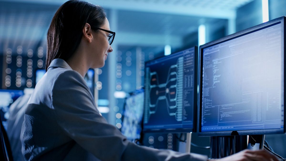 A woman analyzing data on dual monitors in a high-tech office.